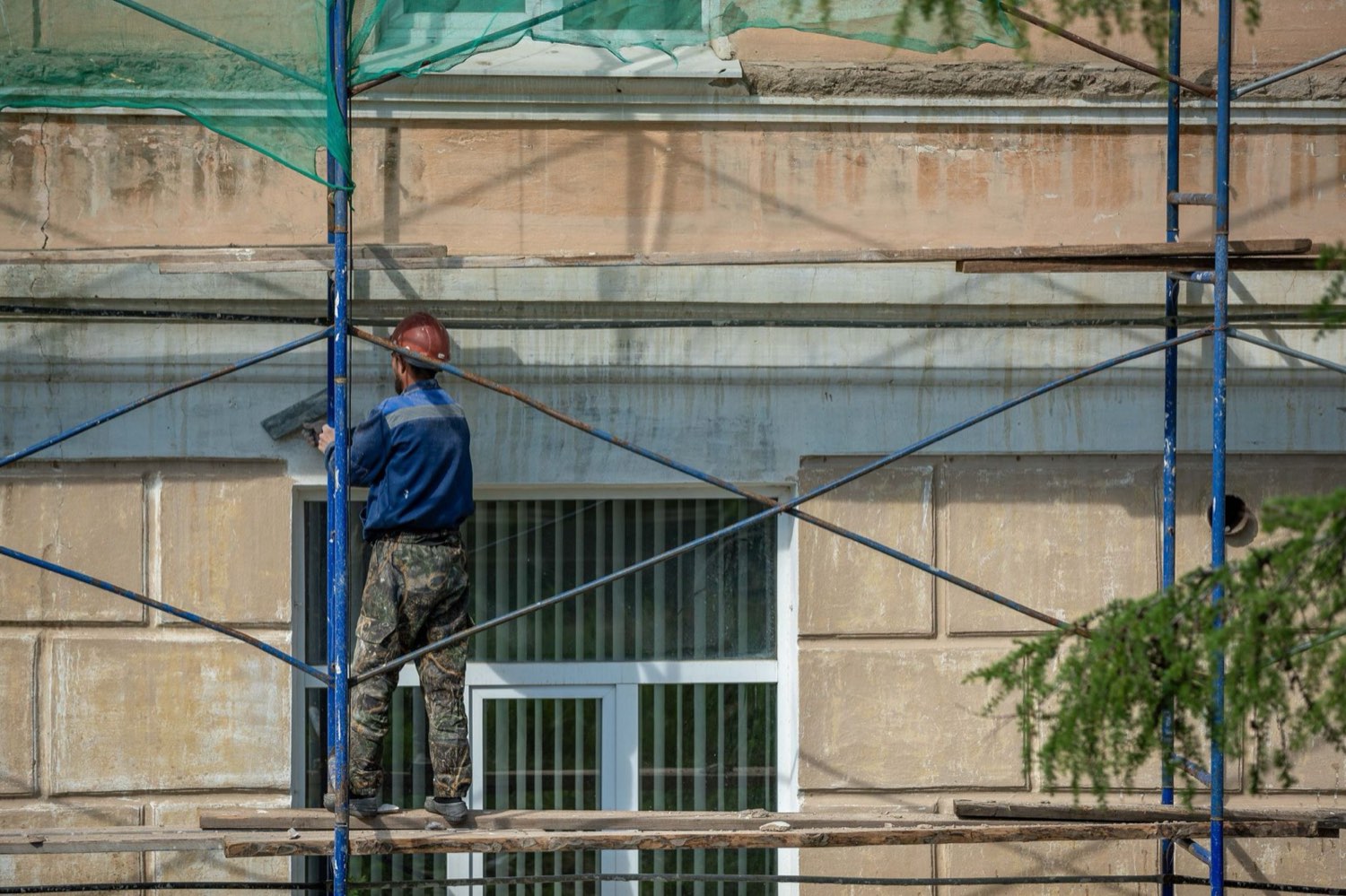Murár na lešení pri fasáde rodinného domu